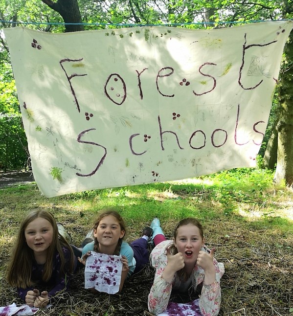 Three girls with a handmade forest school sign above them